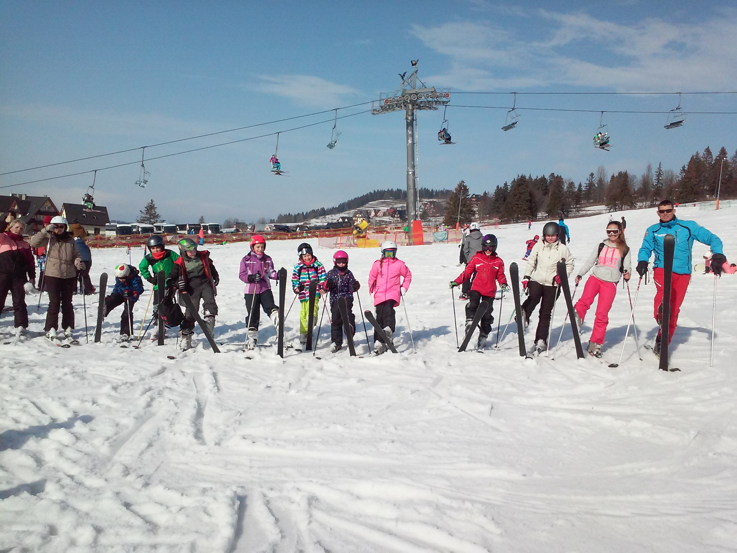 Duża grupa uczestników obozu zimowego na stoku, z nartami